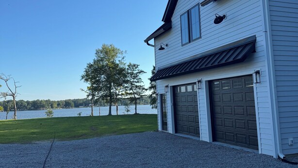 A two-story house with a garage, a gravel driveway, and a view of a lake.