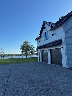 A two-story house with a garage, a gravel driveway, and a view of a lake. - Charming new in 2026 private apartment on the water in lovely Edenton. (Edenton)