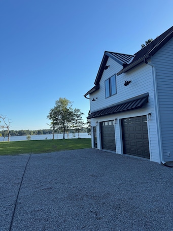 A two-story house with a garage, a gravel driveway, and a view of a lake.. Charming new in 2026 private apartment on the water in lovely Edenton.