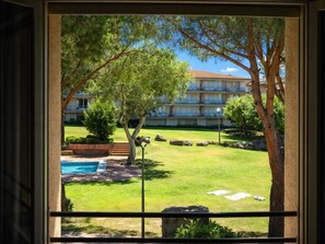 Blick durch ein Fenster auf einen Hotelinnenhof mit Schwimmbad, Bäumen und einem Gebäude mit Balkonen.