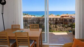 Un comedor con mesa y sillas, un sofá y vista al mar a través de un cerrojo corredizo.