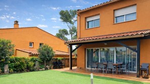 A two-story house with a patio area, a covered outdoor seating area, and a well-maintained lawn. - Family home 50m from the beach - 8 guests (Palamós)