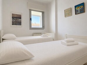 A hotel room with two beds, a window, and artwork on the walls. - Apartment with sea view in La Fosca - details coming soon (Palamós)