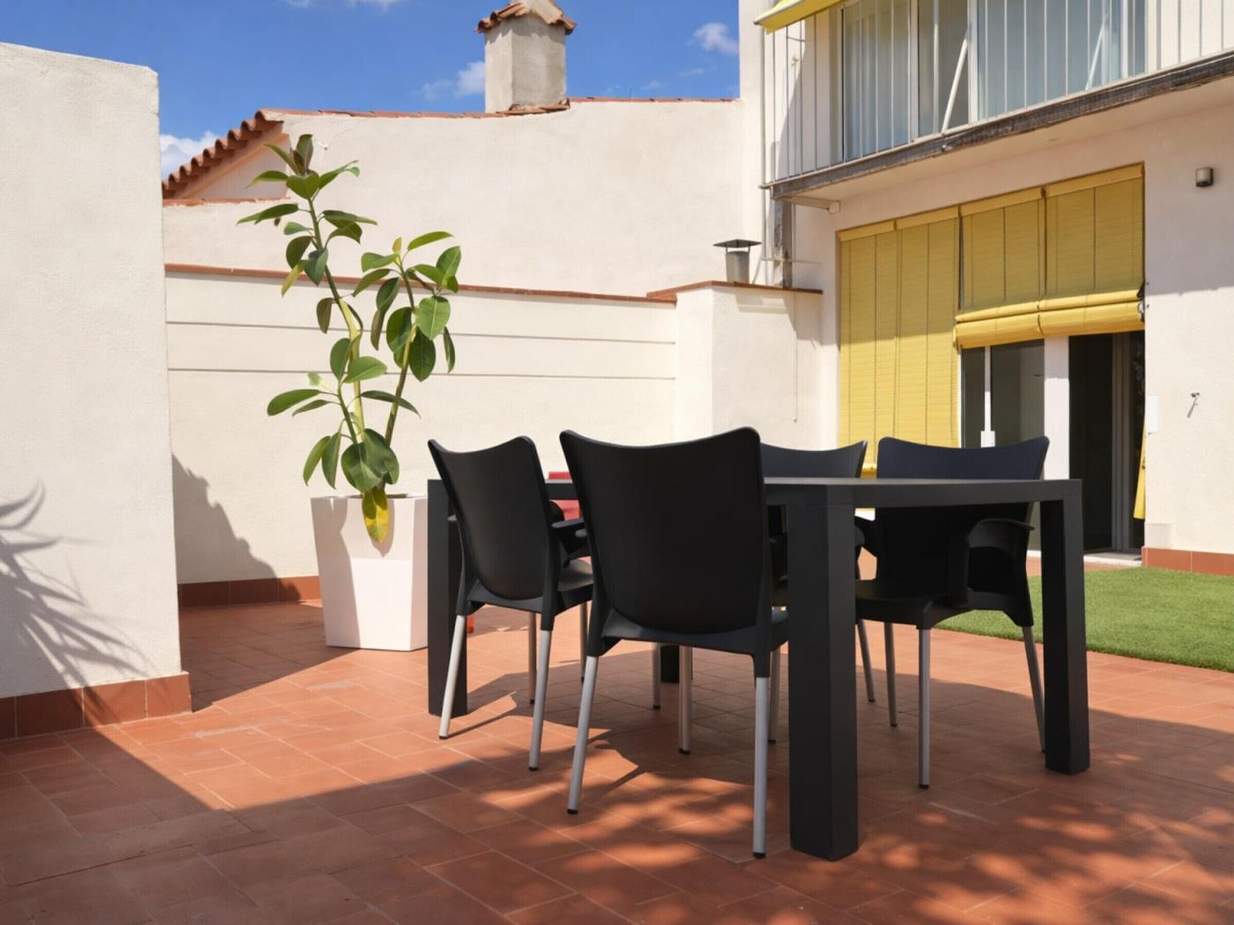 Een terras buiten met een tafel, stoelen, een potplant en een geel zonnescherm.