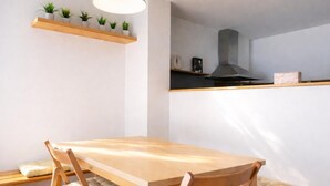 Un coin repas avec une table et des chaises en bois, un luminaire suspendu et une cuisine en arrière-plan.