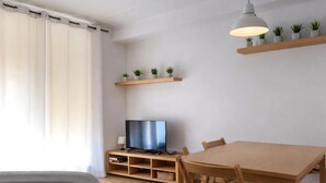 Un salon moderne avec un téléviseur, une table à manger en bois, des chaises, une bibliothèque et un luminaire au plafond.