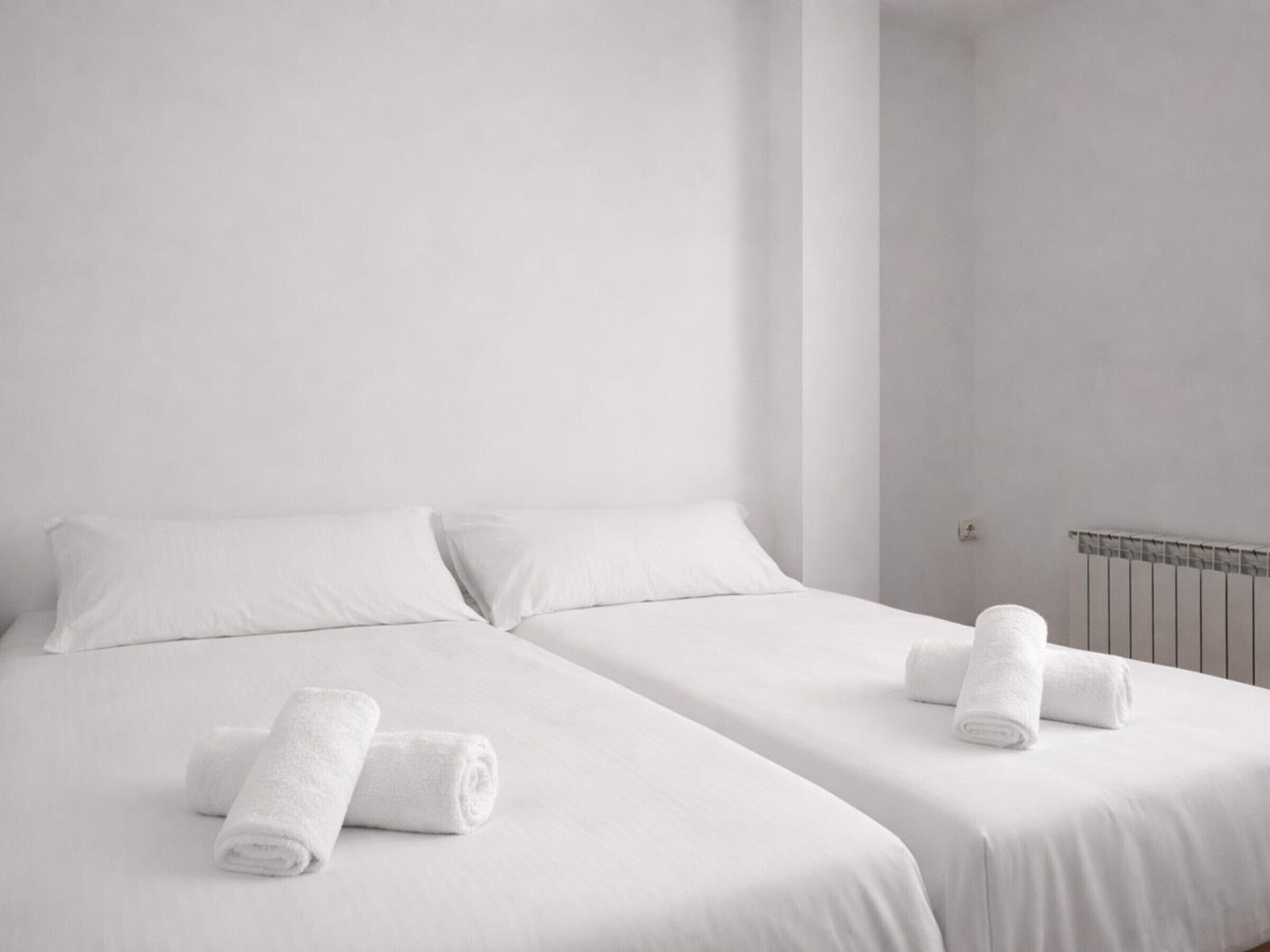 Une chambre d’hôtel avec deux lits simples, du linge de lit blanc et des serviettes enroulées.
