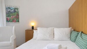 Una cama bien hecha con sábanas blancas, una lámpara de noche y un cartel en la pared.