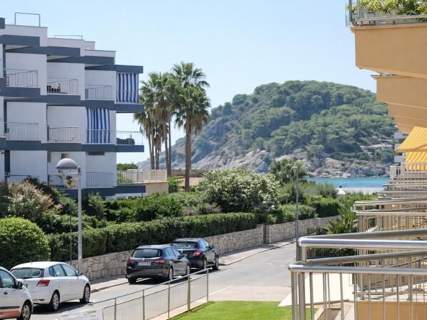 Un bâtiment moderne doté de balcons, une route où circulent des voitures et une vue sur un paysage montagneux.