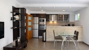 Een moderne keuken met inbouwapparatuur, een eethoek met een glazen tafel en een aan de muur bevestigde televisie.