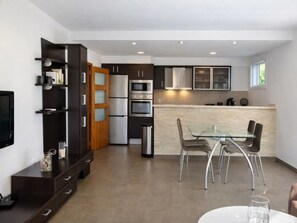 A modern kitchen with built-in appliances, a dining area with a glass table, and a TV mounted on the wall. - Cozy apartment in La Fosca, private parking (Palamós)