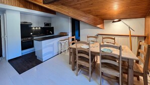 Una cocina moderna con microondas, horno y estufa negra, un comedor con sillas de madera y una mesa, y un tragaluz arriba.