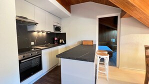Una cocina moderna con encimera negra, armarios blancos y techo de madera.