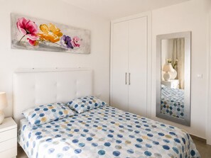 Ein Schlafzimmer mit Bett, Nachttisch, Kommode, Kleiderschrank, Spiegel und einem floralen Gemälde an der Wand.