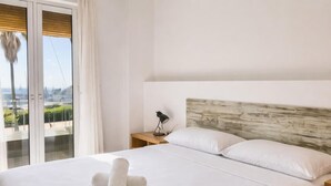 A hotel room with a large bed, a wooden headboard, a nightstand with a lamp, and a view of the city through the window.