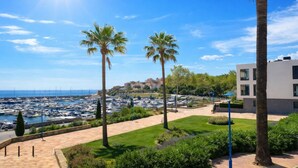 A marina with boats, palm trees, and a modern building with a flat roof.