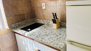 A kitchen with a granite countertop, a black induction cooktop, a knife block, and a white refrigerator.
