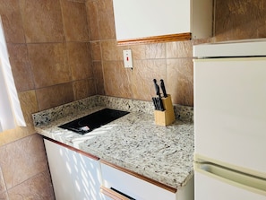 A kitchen with a granite countertop, a black induction cooktop, a knife block, and a white refrigerator. - Lovely 1-bedroom Super Studio with AC in charming Ocho Rios's, Jamaica St Ann. (Ocho Rios)