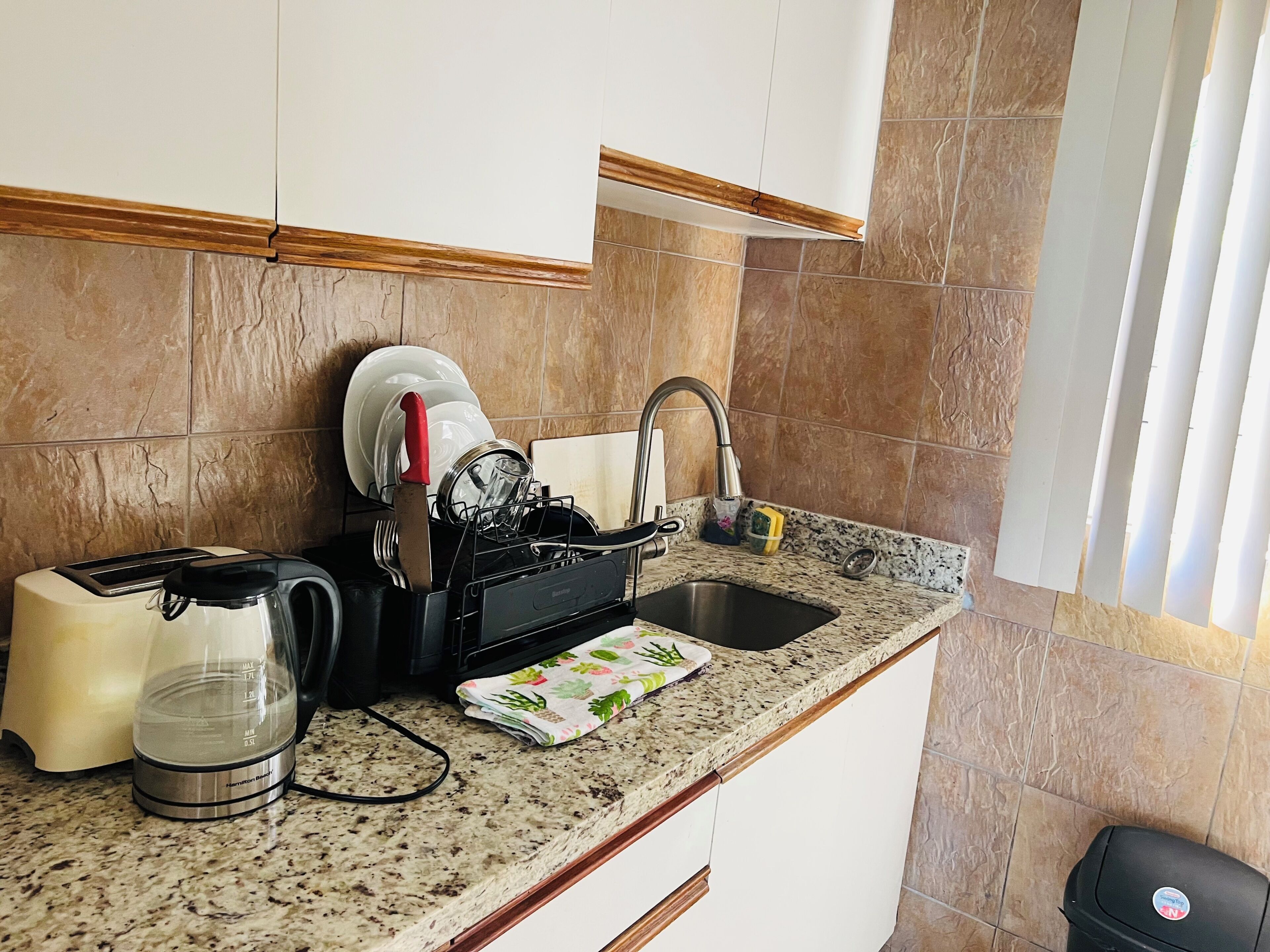 A kitchen with a granite countertop, a coffee maker, a toaster, a sink, and a dish rack.