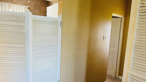 A hallway with closed white shutters, a tiled floor, and a door with a light switch.