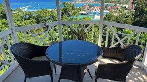 A balcony with a table and chairs, overlooking a coastal view with buildings and greenery.