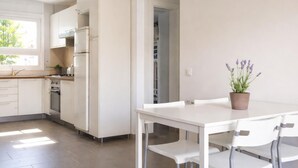 A modern kitchen with white cabinets, a stainless steel stove, and a dining area with a white table and chairs. - Renovated apartment, near beach - 4 guests (Palamós)
