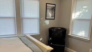 Une chambre à coucher avec un grand lit, une chaise et un tableau encadré accroché au mur.