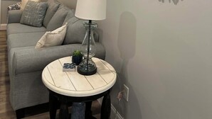 Un salon avec un canapé gris, une table ronde surmontée d’une lampe et une œuvre d’art murale.