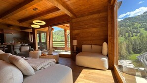 A wooden interior with a sofa, chairs, a dining area, and a large window with a mountain view. - Exceptional Chalet in Vars – 21 guests, 450 sqm, 3 suites (Vars)