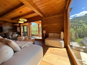 A wooden interior with a sofa, chairs, a dining area, and a large window with a mountain view. - Exceptional Chalet in Vars – 21 guests, 450 sqm, 3 suites (Vars)