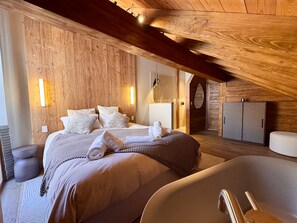 A bedroom with a wooden ceiling, a bed with white linens, a large window, and a bathtub. - Exceptional Chalet in Vars – 21 guests, 450 sqm, 3 suites (Vars)