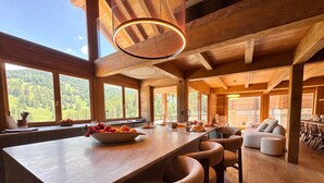 A wooden interior with a central bar area, seating, and large windows offering a view of a forested landscape. - Exceptional Chalet in Vars – 21 guests, 450 sqm, 3 suites (Vars)