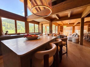 A wooden interior with a central bar area, seating, and large windows offering a view of a forested landscape. - Exceptional Chalet in Vars – 21 guests, 450 sqm, 3 suites (Vars)