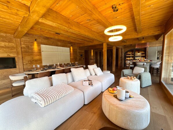 A modern interior with a wooden ceiling, a large sofa, a dining area, and a kitchen. - Exceptional Chalet in Vars – 21 guests, 450 sqm, 3 suites (Vars)