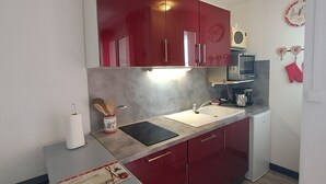 Una cocina compacta con armarios rojos, un microondas, un lavamanos y un refrigerador pequeño.