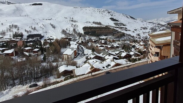 Un pueblo cubierto de nieve en la montaña, con edificios, un telesilla y un cielo despejado.