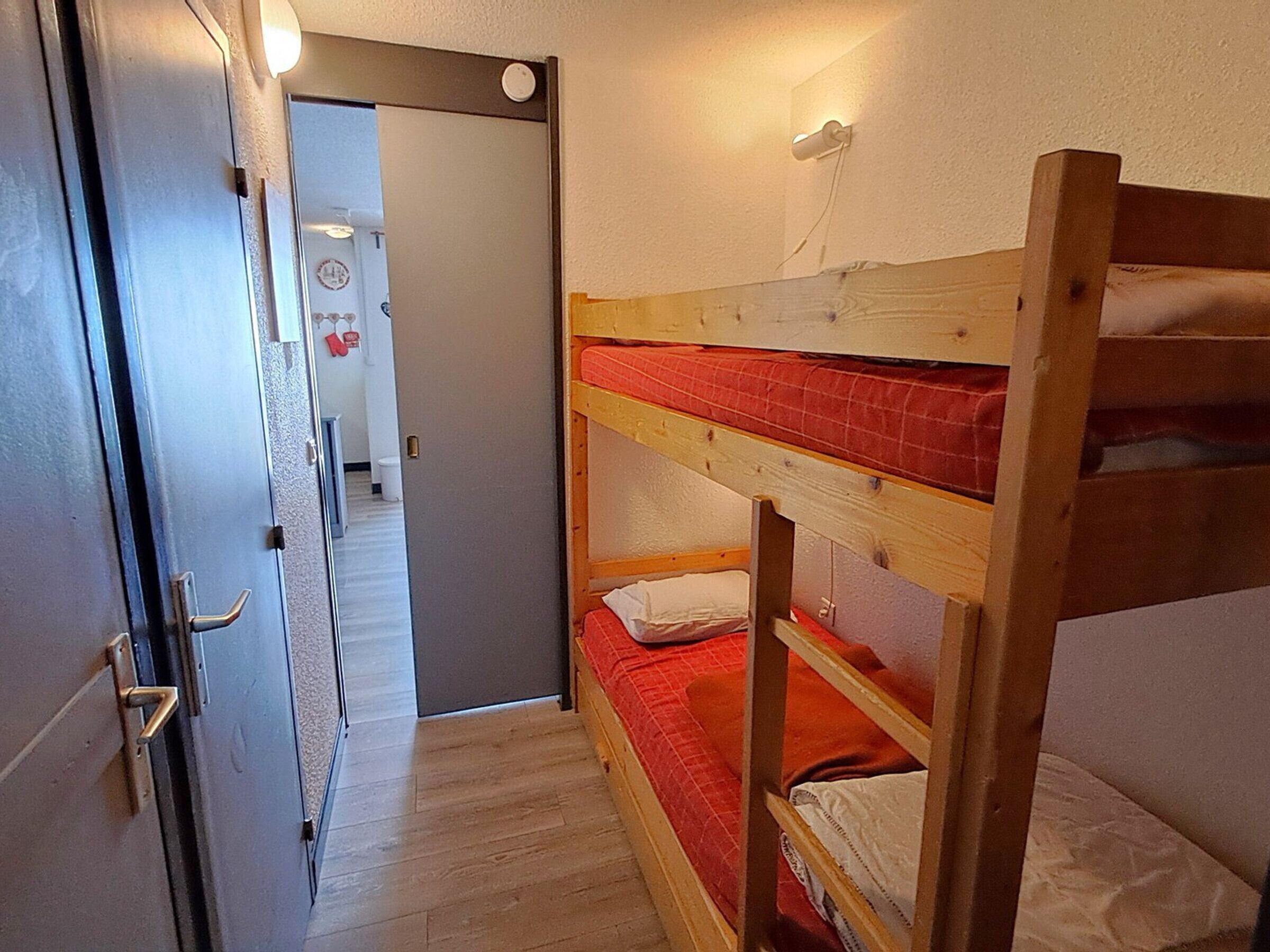 Une chambre avec un lit superposé, une porte, un interrupteur et une prise électrique au mur.
