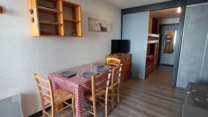 Habitación compacta con una mesa de comedor dispuesta para cuatro personas, una televisión y una cama litera al fondo.