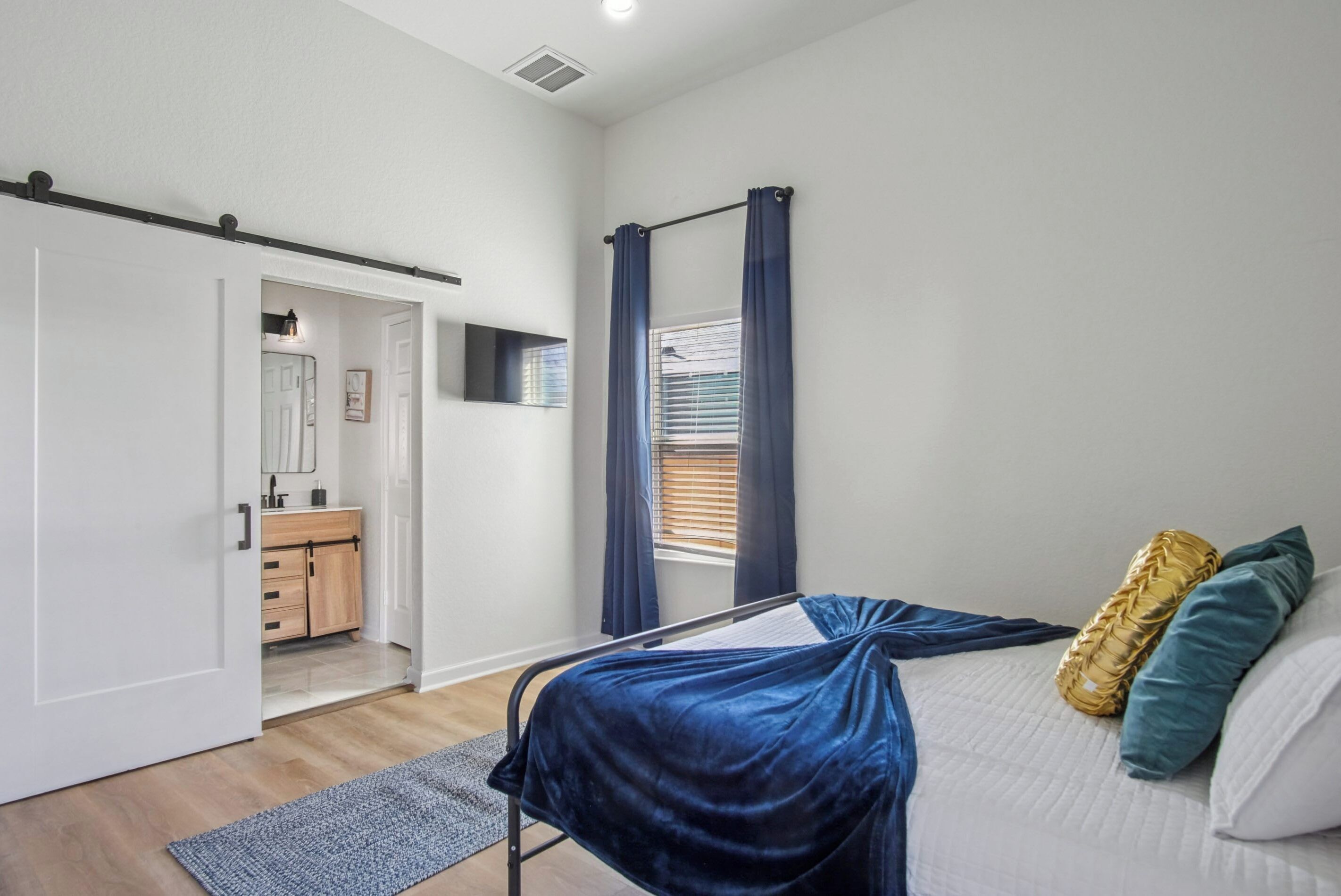 A bedroom with a bed, a wardrobe, a bathroom, and a window with curtains.