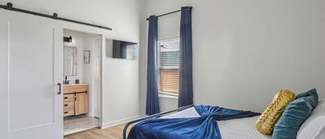 A bedroom with a bed, a wardrobe, a bathroom, and a window with curtains.