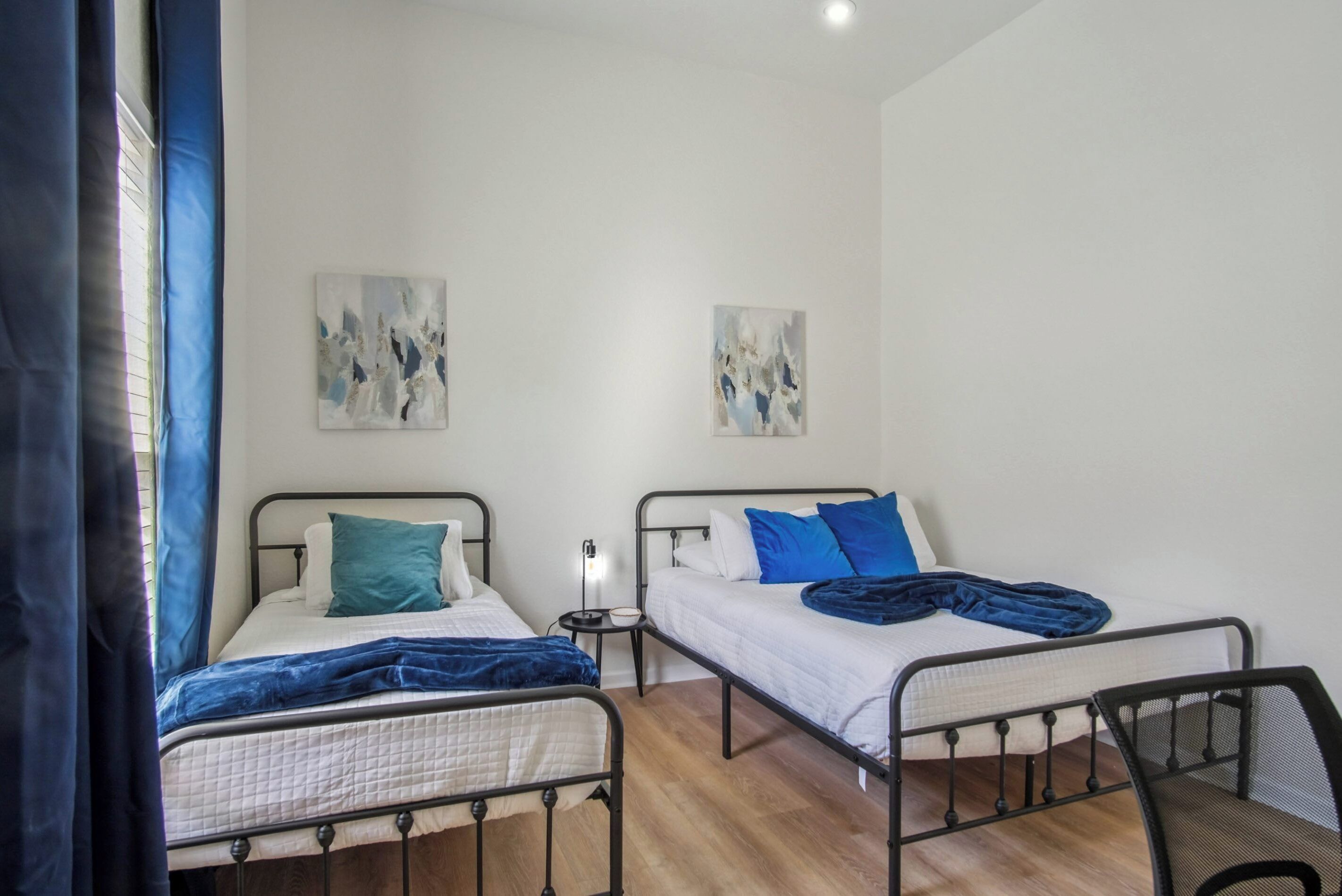 A room with two beds, a small table, and abstract art on the walls.