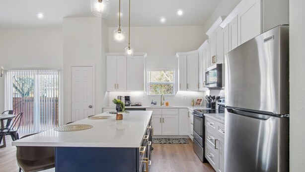 A modern kitchen with white cabinets, a stainless steel refrigerator, and pendant lighting. - Elegant 4br/3ba Gem Near Downtown & The Alamo (San Antonio)