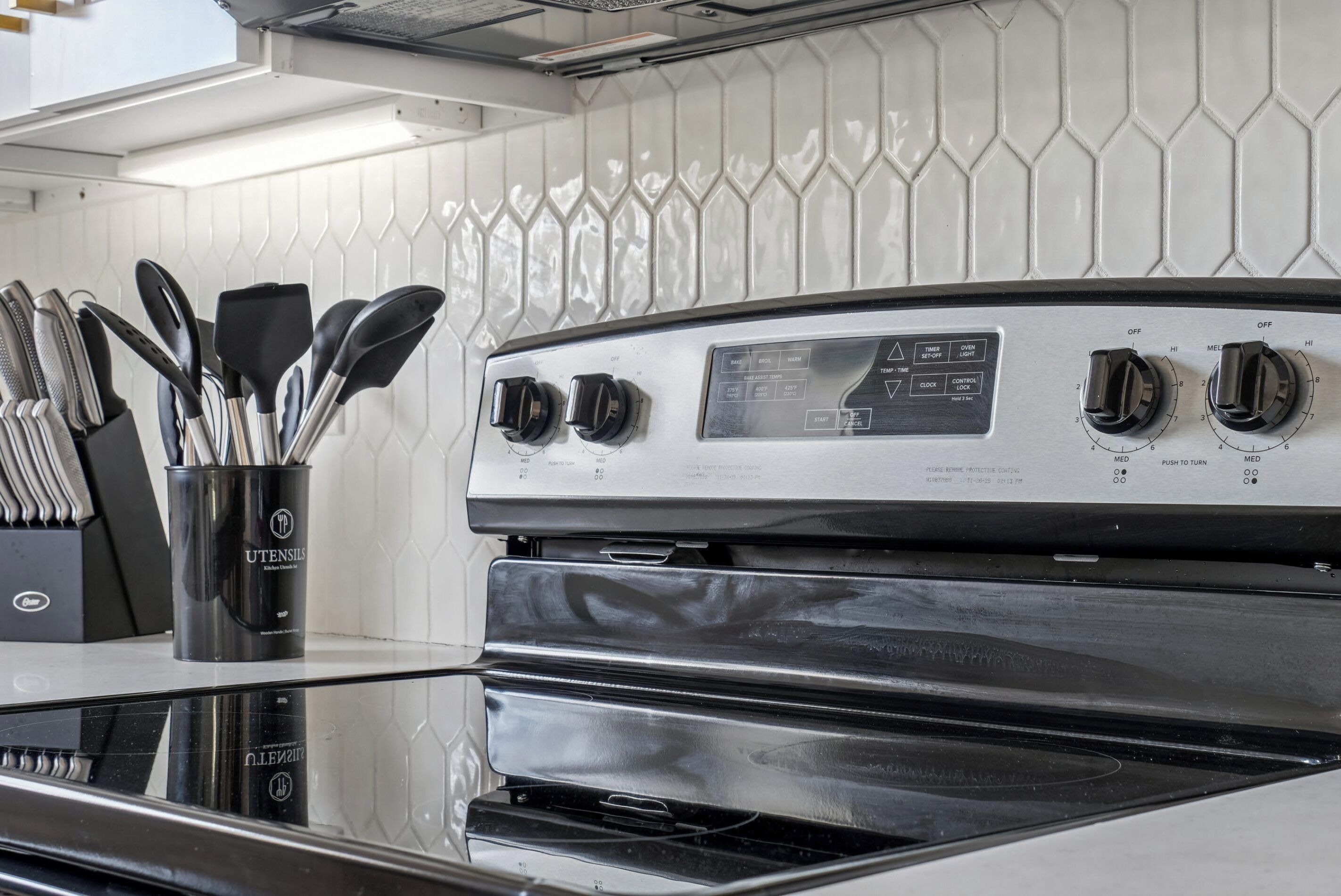 A kitchen with a stainless steel stove, a utensil holder, and a white tiled backsplash.