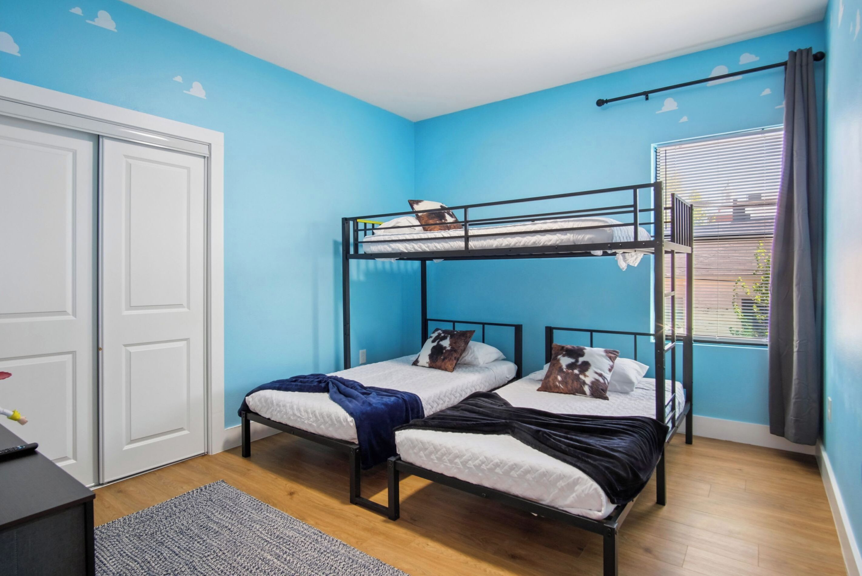 Une chambre avec un lit superposé, un bureau, une fenêtre avec des rideaux et une porte.