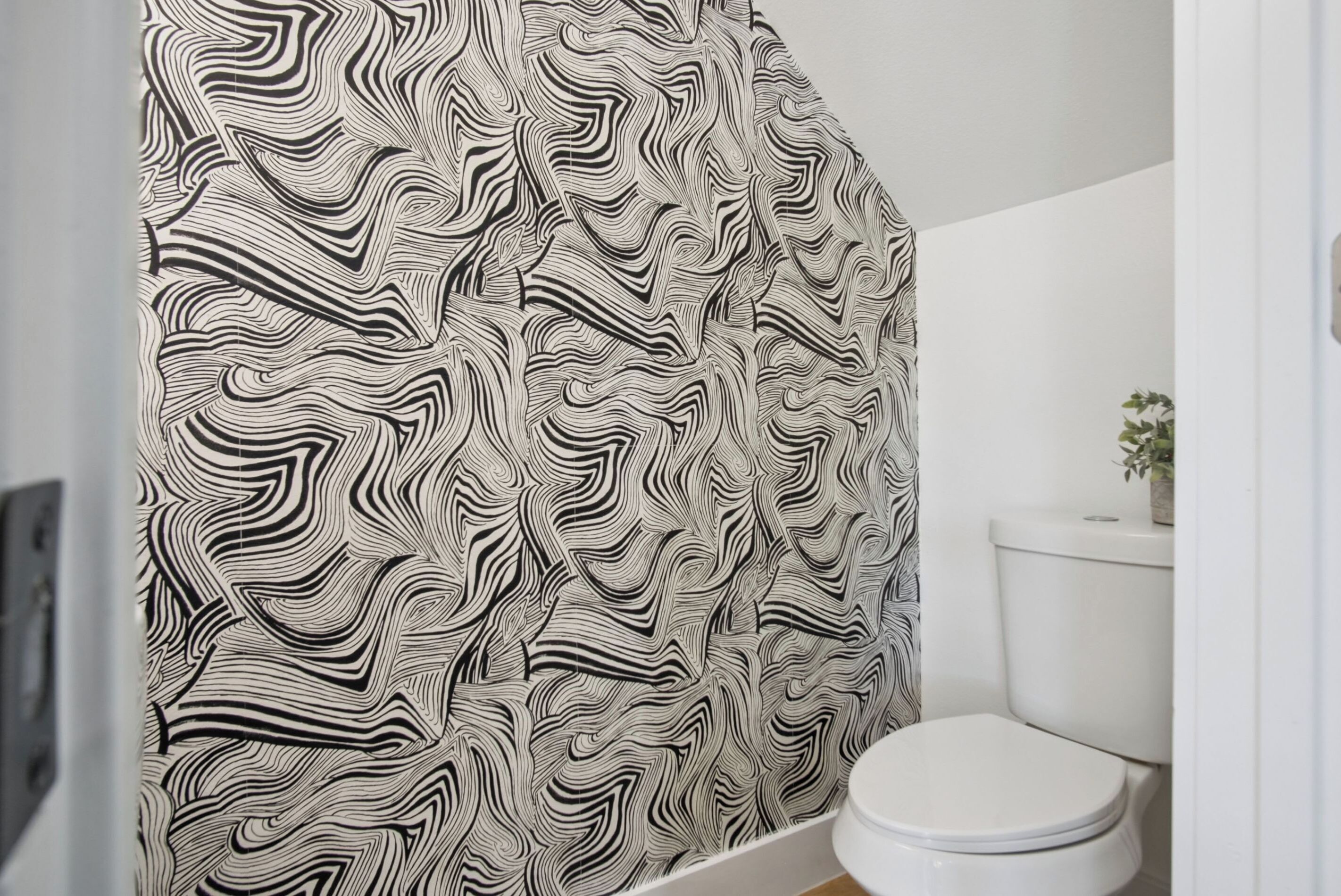 A bathroom with a patterned shower curtain, a white toilet, and a small plant on the tank.