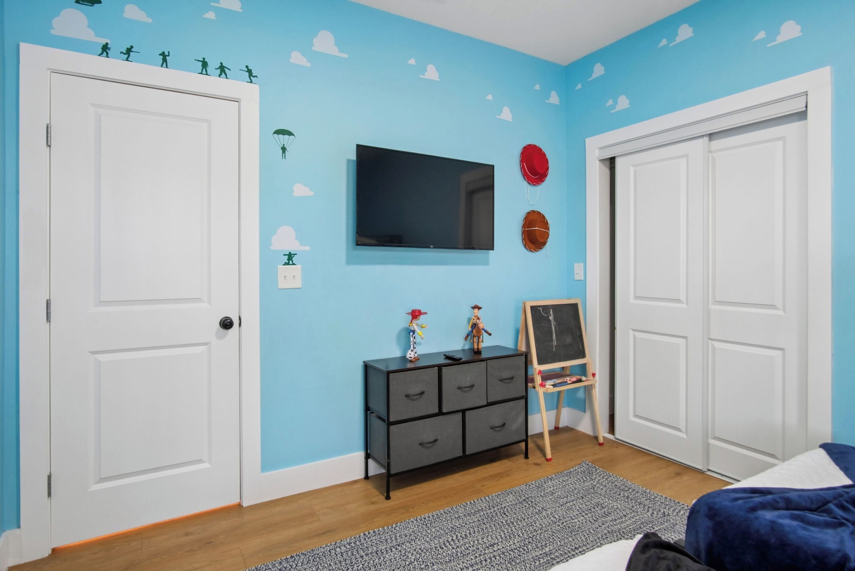Ein Zimmer mit blauer Wand, weißen Türen, einem schwarzen Fernseher, einer kleinen schwarzen Kommode und einer Tafel.