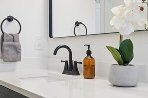 A bathroom with a white sink, black faucet, and a potted orchid. - Stylish Downtown Retreat Near the Alamodome (San Antonio)