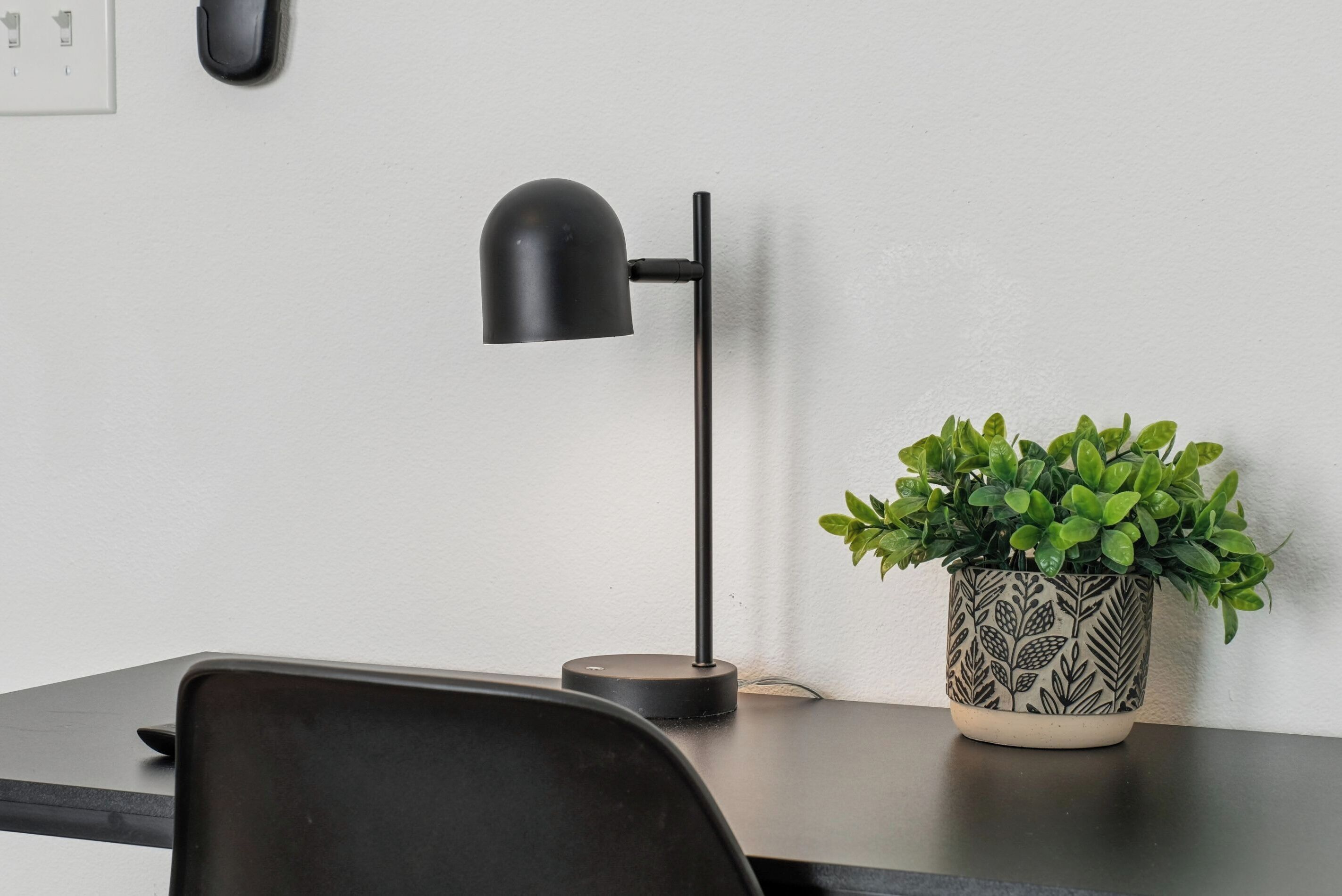 Una scrivania con una lampada da tavolo nera, una pianta in vaso e una sedia nera.