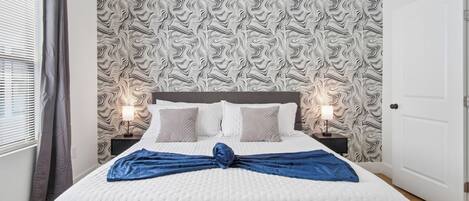 A neatly made bed with a blue towel, two bedside lamps, and a patterned wallpaper.