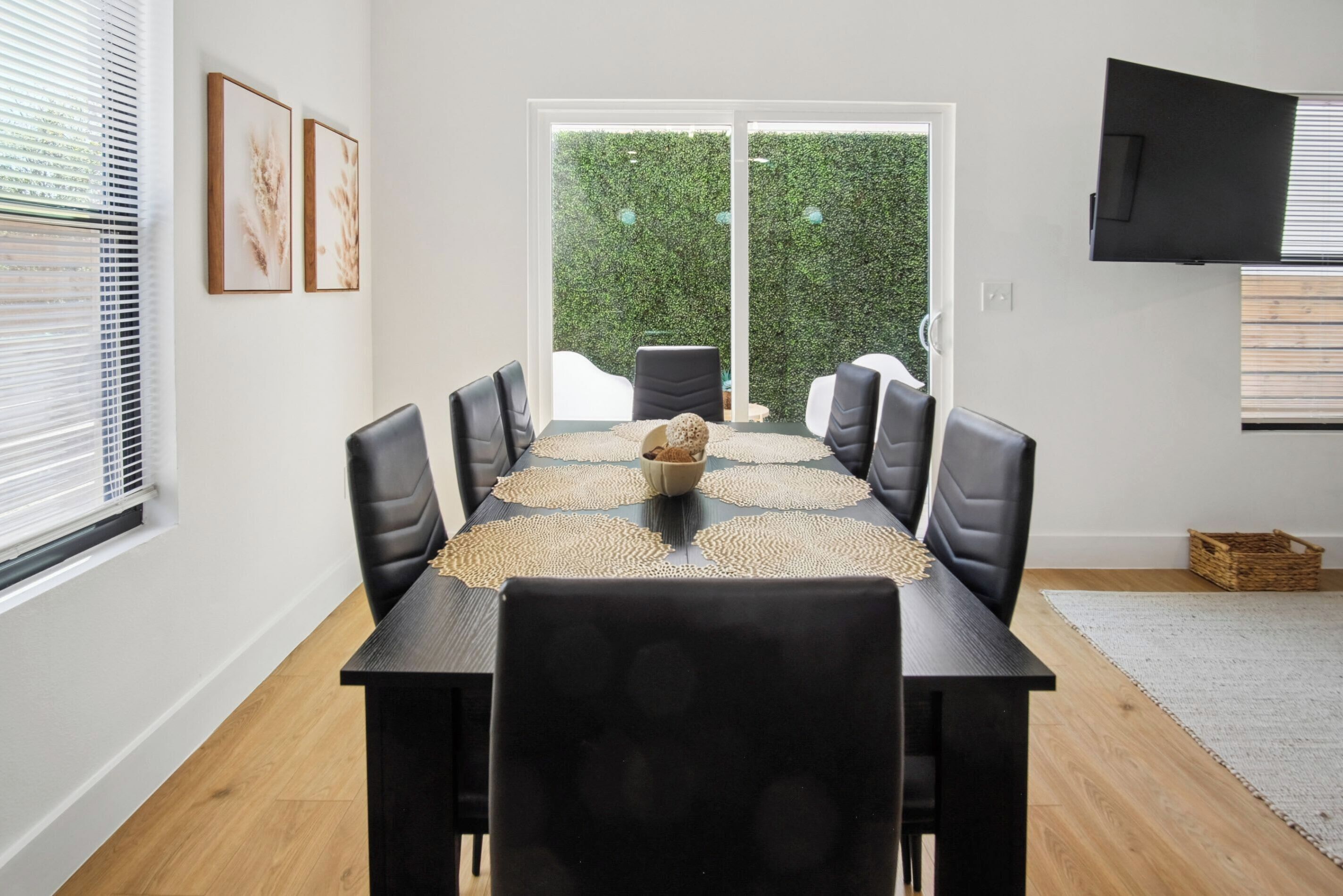 A dining area with a table set for six, black chairs, a woven placemat, and a bowl of fruit.